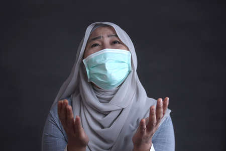 Asian female muslim crying and pray to God against coronavirus covid 19 pandemic disease. Stress in lockdown quarantine conceptの写真素材