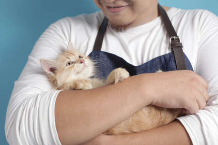 Happy Asian man smiling while holding his kitten. Animal lover with his cat pet concept, against...