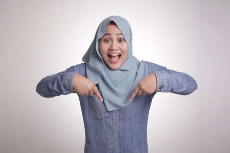 Portrait of Asian muslim woman surprised and pointing down isolated on whiteの写真素材