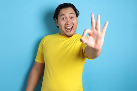 Young Asian man shows okay OK sign. Close up body portrait against white wall