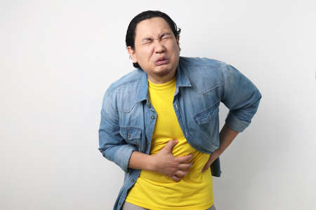Portrait of young Asian man squezze his stomach for having stomachache pain