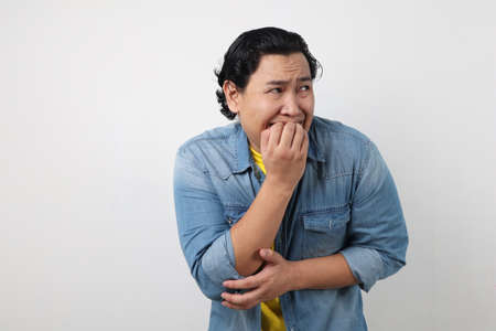 Portrait of young funny Asian man biting his nails as if he is worried afraid of something badの写真素材