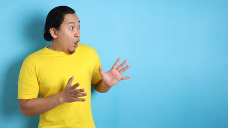 Portrait of young Asian man shocked to see something on his side, excited gesture with copy spaceの写真素材
