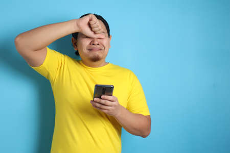 Attractive young Asian man reading texting chatting  on his phone, bad news, sad  crying expression