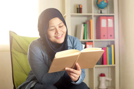 Portrait of young muslim businesswoman wearing hijab reading book inside her home, during covid 19 stay home quarantine lockdown, stay healthy and happyの写真素材
