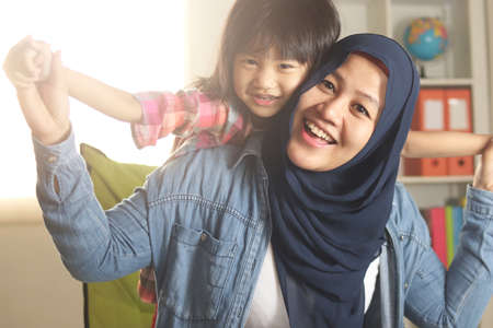Muslim mother wearing hijab smiling while playing with her baby girl, mom and daughter love each other, happy single parentの写真素材
