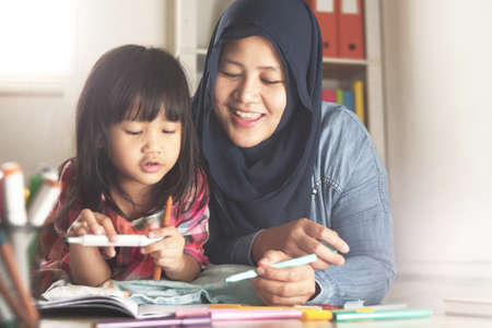 Asian muslim mother drawing with her daughter, single mom teaching baby girl, learning on the floor,...