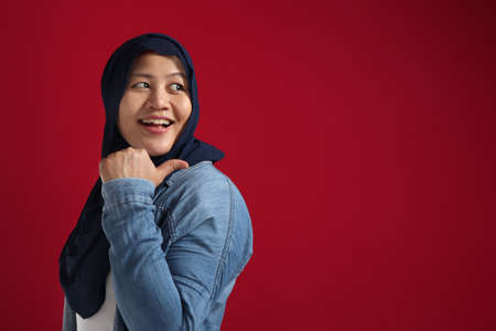 Portrait of Asian young happy muslim woman  pointing to presenting something on her side, against red background with copy spaceの写真素材