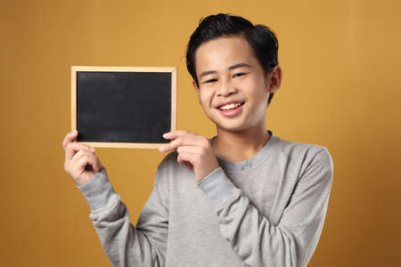 Portrait of smart young cute Asian boy smiling at camera while holding and showing empty blackboard...