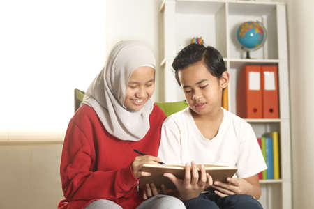 Kids learning together, muslim sister wearing hijab help or teach her little brother to do home work, education and happy family conceptの写真素材
