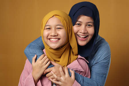 People and family, happy smiling Asian muslim mother hugging daughter against yellow background, motherhood conceptの写真素材