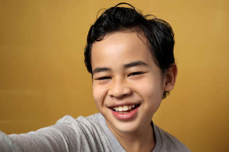 Close up of young little Asian kid taking a selfie photo over yellow background, shows happy smiling cheerful expression の写真素材