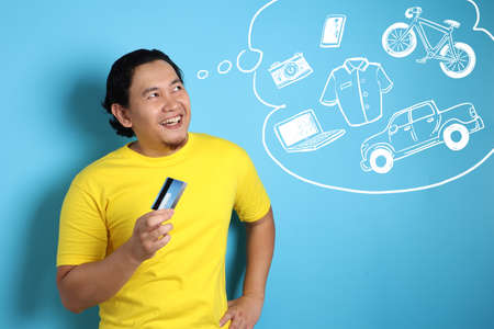 Portrait of happy young Asian man smiling and thinking to buy a lot of things while holding a credit...