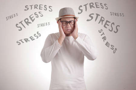Stress. Asian man close his eyes and hold his head, due to stress against white backgroundの写真素材