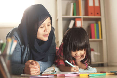 Asian muslim mother drawing with her daughter, single mom teaching baby girl, learning on the floor, happy family conceptの写真素材