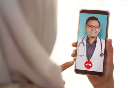 Concept of online medical healthcare services, shows smartphone app with Asian male doctor smiling, telehealth, telemedicine video callの写真素材
