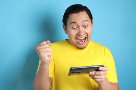 Photo image portrait of a cute handsome young Asian man with funny face playing games on tablet...