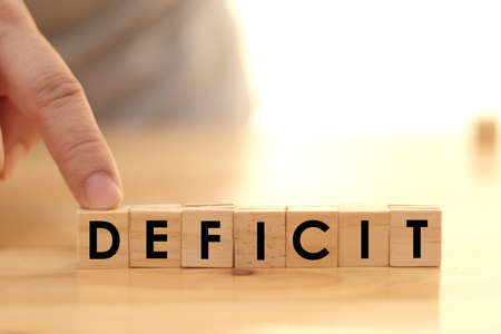 Deficit writing on wooden cube blocks, word text typography arrange on wood table by one businessmanの写真素材
