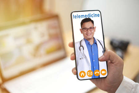 Concept of online medical healthcare services, shows smartphone app with Asian male doctor smiling, telehealth, telemedicine video callの写真素材