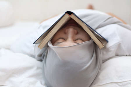 Asian muslim woman slept with book covering on her face, tired college student studying late until midnight conceptの写真素材