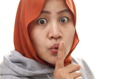 Asian muslim woman asking for silent, finger over lip, shushing gesture, isolated on white