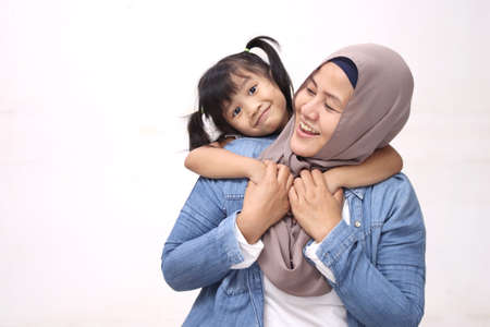 Muslim mother wearing hijab smiling while playing with her baby girl, mom and daughter love each...