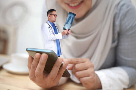 Concept of online medical healthcare services, shows smartphone app with Asian male doctor checking x-rays and smiling woman, telehealth, telemedicine video callの写真素材