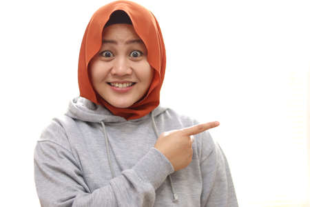 Portrait of Asian young happy muslim woman smiling and pointing to presenting something on her side, isolated on white with copy spaceの写真素材