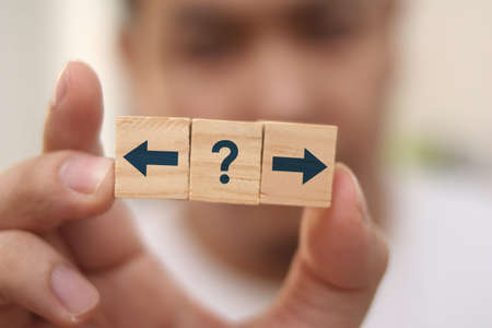 Choosing direction concept, man holding wooden block with arrow and question mark symbol, selective...
