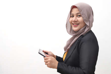 Muslim business woman wearing hijab holds and using smart phone or digital tablet. Successful businesswoman entrepreneur and internet gadget concept, side view portrait isolated on whiteの写真素材