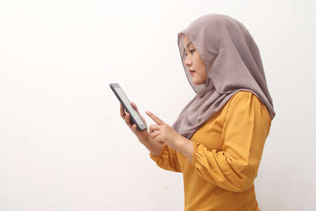 Muslim business woman wearing hijab holds and using smart phone or digital tablet. Successful businesswoman entrepreneur and internet gadget concept, side view portrait isolated on whiteの写真素材
