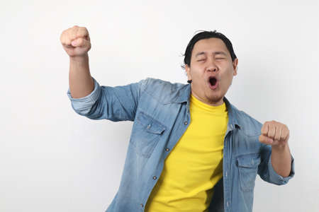 Portrait of a funny young Asian man smiling and dancing happily, joyful expressing celebrating good...