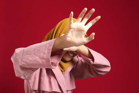Young muslim teenage girl wearing hijab crying and covering her face, afraid worried expression,...