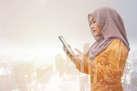 Muslim business woman wearing hijab holds and using smart phone or digital tablet. Successful businesswoman entrepreneur and internet gadget concept, multiple expoureの写真素材