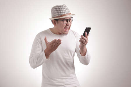 Attractive young Asian man talking on his phone, getting bad news, shocked mad angry gestureの写真素材