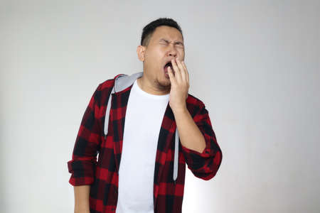 Sleepy tired funny young Asian man yawning, sleeping while standing, half body portrait over white...