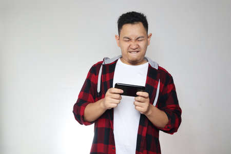 Portrait of a cute handsome young Asian man with funny face playing games on tablet smart phone