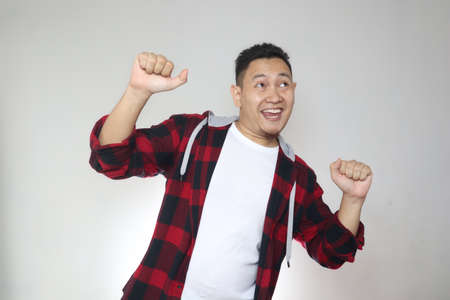 Funny young Asian man smiling and dancing happily, joyful expressing celebrating good news victory winning success gestureの写真素材