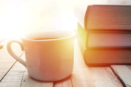 Cup of latte or cappuccino coffee with a stack of books in coffee shop with sun light effect