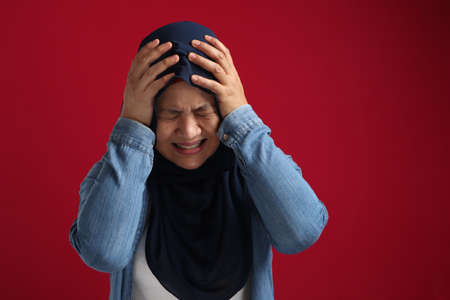 Portrait of Asian muslim lady wearing hijab hold her head in pain for having headache, stress or sad...