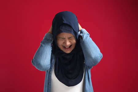 Portrait of muslim lady wearing red hijab having headache, migraine chronic head brain pain or stress mental pressure conceptの写真素材