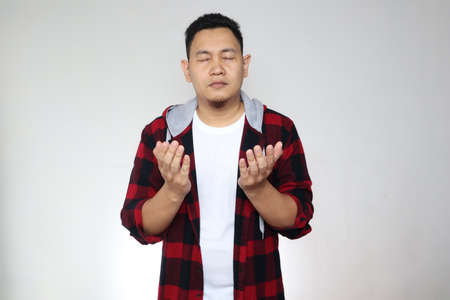 Asian muslim man making pray gesture, hands raised up, eyes closed. Spiritual person conceptの写真素材