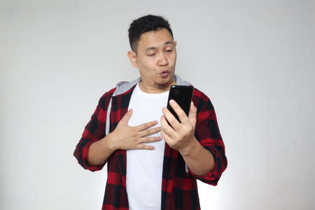 Portrait of young funny Asian man looking at his phone with naughty expression, foundの写真素材
