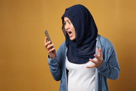 Asian muslim woman angry by phone call, screaming on her phone, over yellow backgroundの写真素材