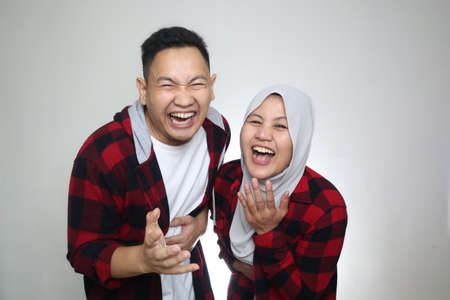 Funny Asian muslim couple, husband and wife laughing hard to camera, bully or joking expression, over grey backgroundの写真素材
