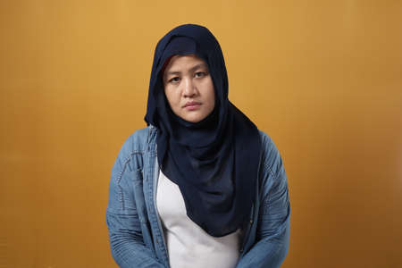 Portrait of sad Asian muslim woman crying against yellow background, sadness depression hopeless conceptの写真素材