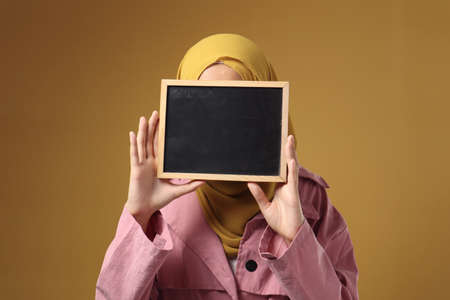 Muslim woman wearing hijab covering her face with blackboard, anonymouse facial expression, blank copy space templateの写真素材