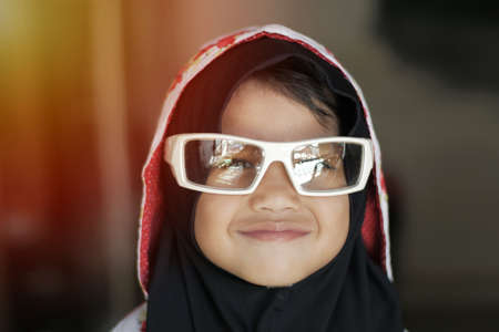 Cute adorable little baby girl looking at camera and smiling, happy Asian muslim girl wearing sunglasses, close upの写真素材