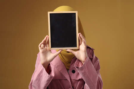Muslim woman wearing hijab covering her face with blackboard, anonymouse facial expression, blank copy space templateの写真素材