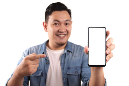 Portrait of young young Asian man presenting smart phone mockup with happy cheerful expression, pointingの写真素材